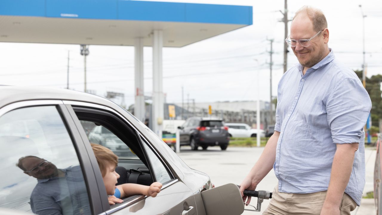 Man at a petrol station filling up a car with a child inside
